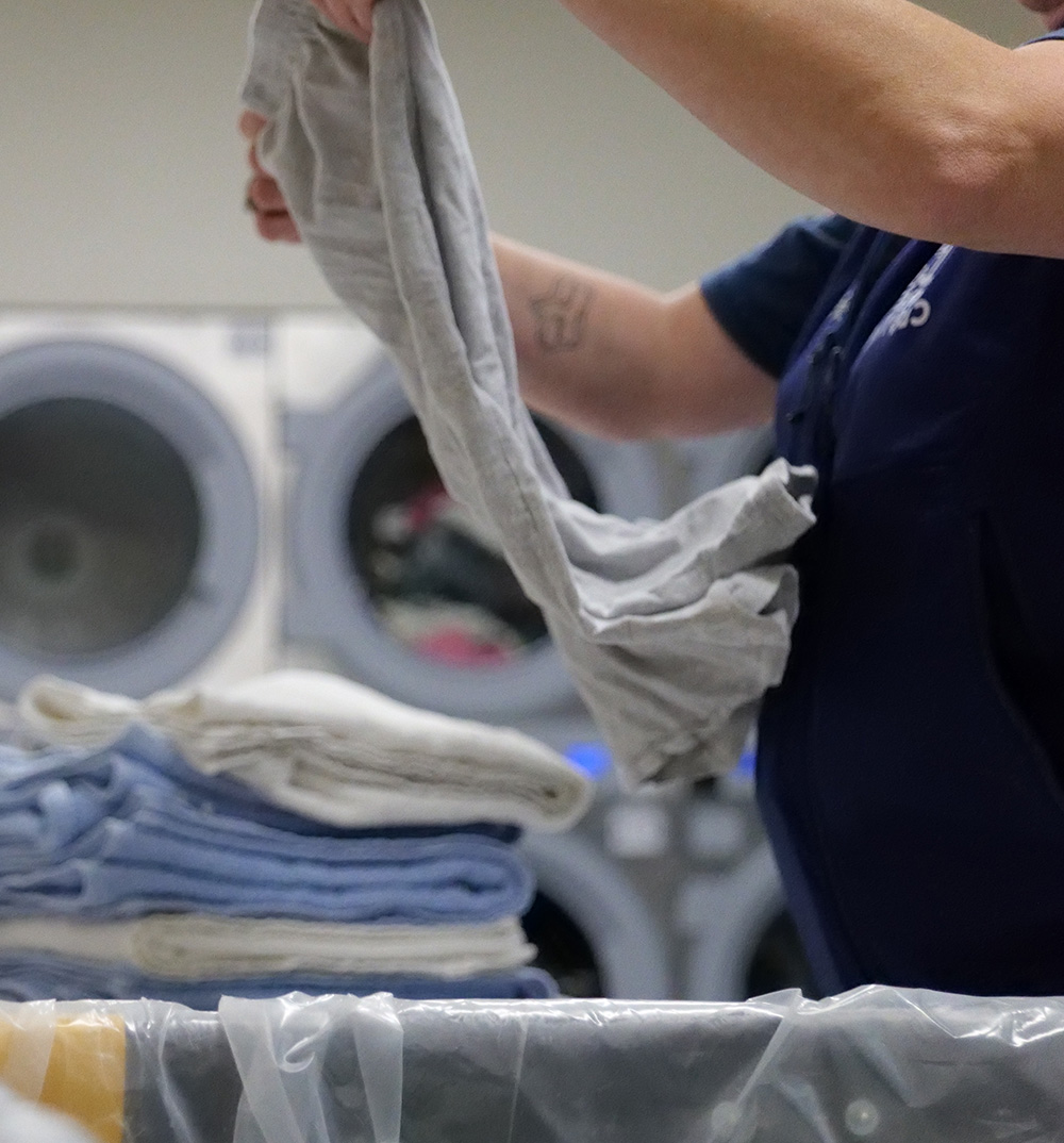 A Fresh Clothes Mobile Laundry staff member folding clinical laundry